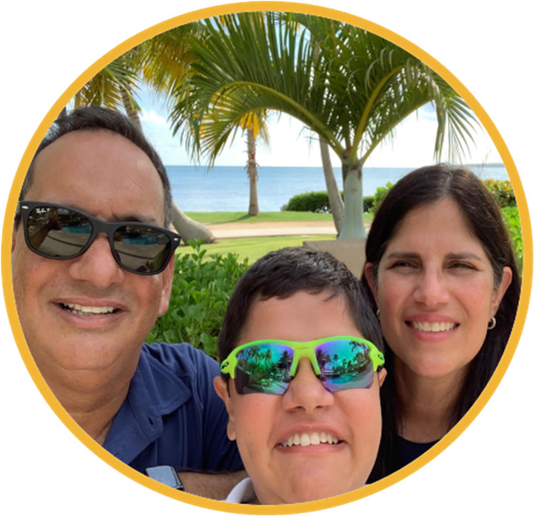 Image of three people up close with palm trees, grass and ocean in the background.